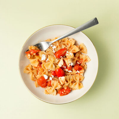 Nudeln mit Feta auf einem Teller mit einer Gabel darin, grüner Hintergrund