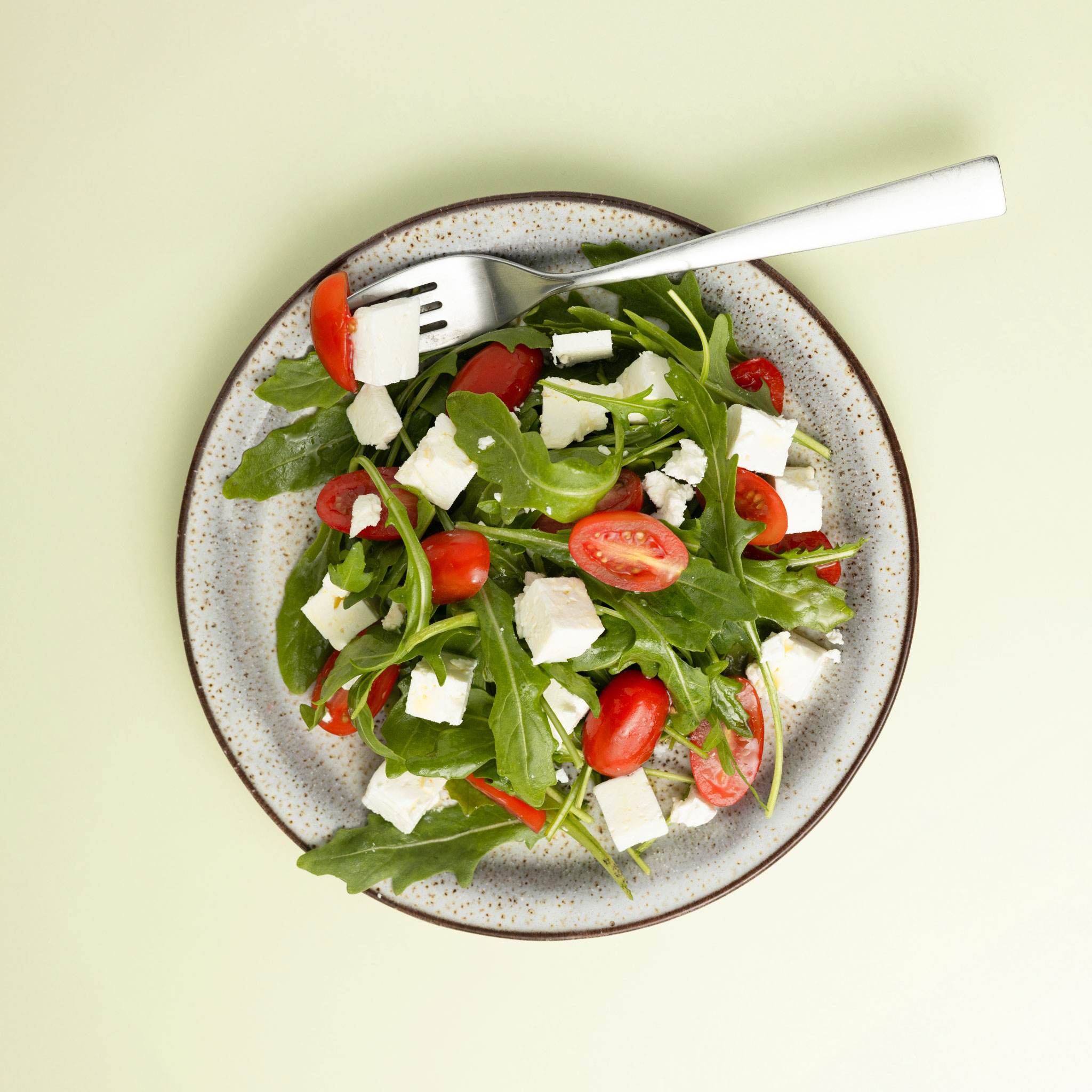Eine Portion Rucola Salat angerichtet auf einem Teller mit grünem Hintergrund