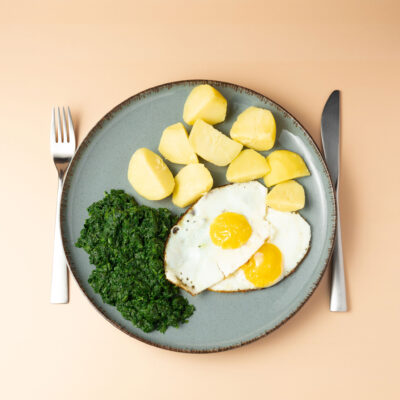 Spiegelei mit Spinat und Kartoffeln auf einem dunkelblauen Teller mit orangefarbenem Hintergrund