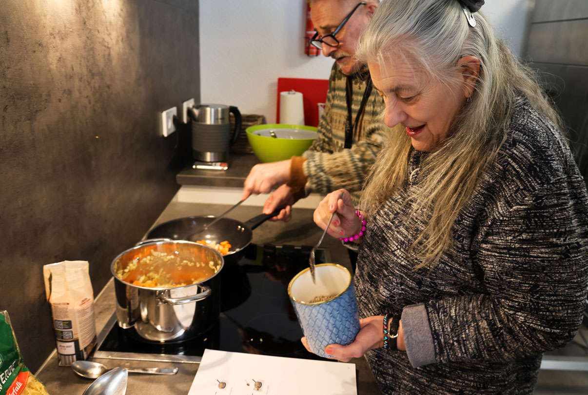 Ein Paar kocht mit dem Kochbuch in Leichter Sprache von Leichtes Kochen, sie stehen in der Küche vor dem Herd