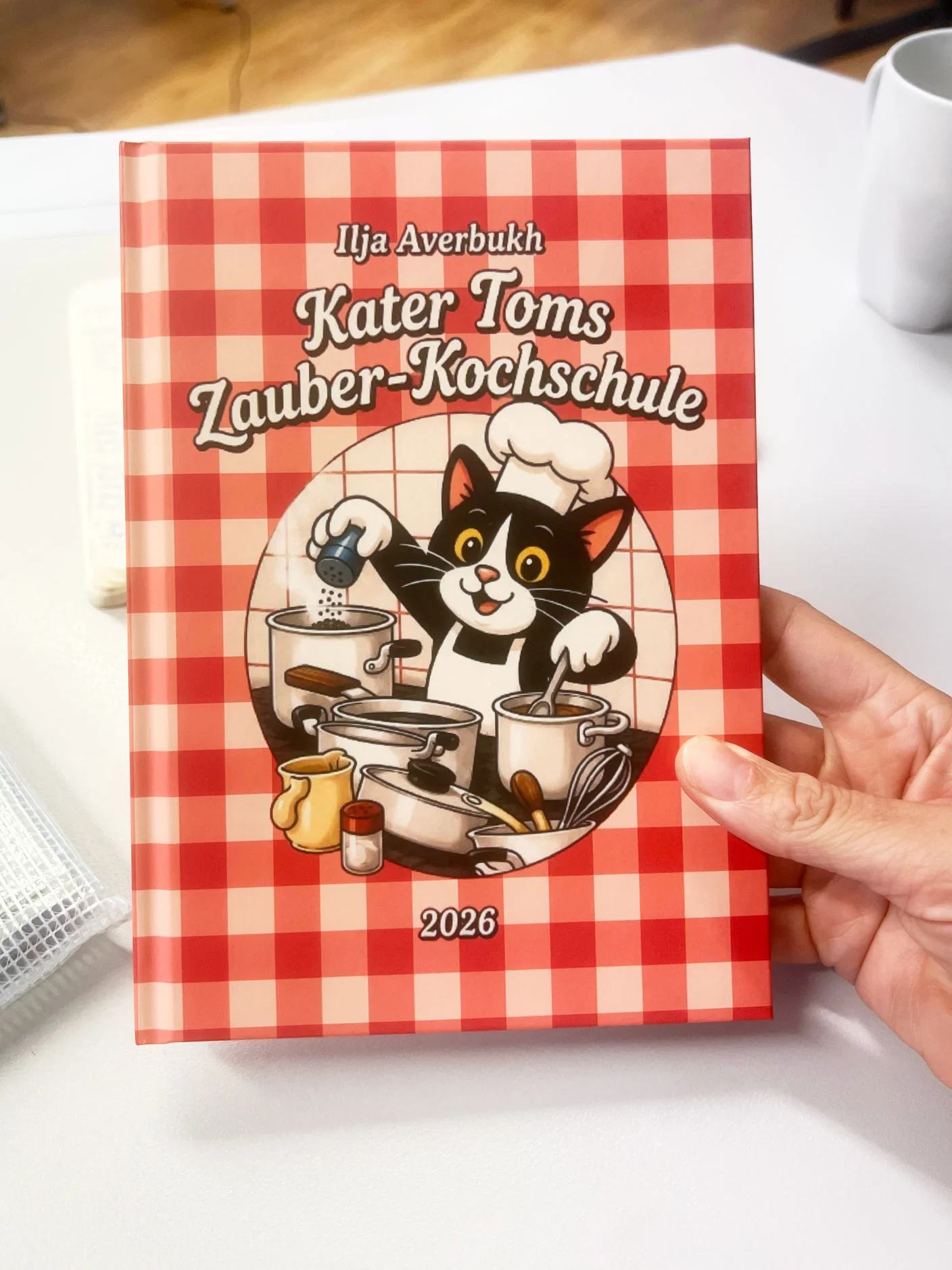 Lebenshilfe Düsseldorf: Das Kater Tom Kochbuch wird von einer Hand ins Bild gehalten