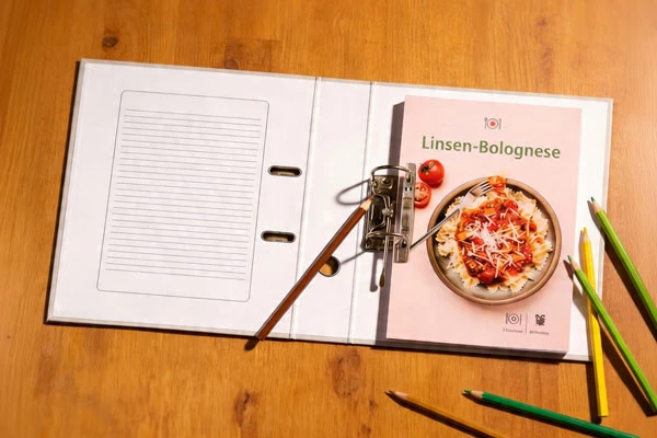 Ein Ringordner liegt auf einem Tisch, darin ist ein Rezept von Leichtes Kochen abgeheftet